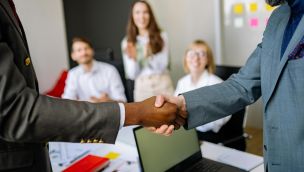 Close-up of a handshake between colleagues in a professional office setting, emphasizing teamwork and agreement.